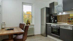 Una cocina moderna con una mesa de comedor, sillas, un refrigerador, un horno, un microondas y un ventanal con vista a árboles.