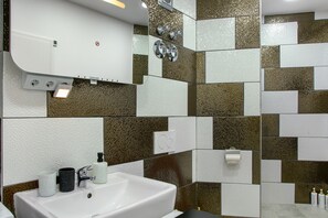 Un baño con un lavamanos blanco, un espejo y una ducha con puerta de cristal.