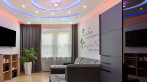 Una sala moderna con un sofá, un televisor, una planta en maceta y una pared con texto decorativo.