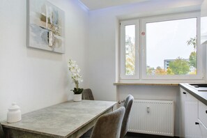A modern kitchen with a window, white walls, and a dining area with a table and chairs.