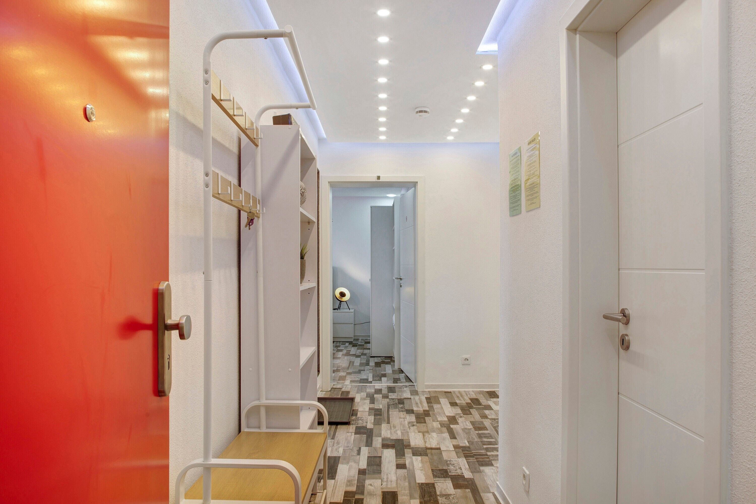 A hallway with a red door, a white door, and a staircase leading to a room with a bed.