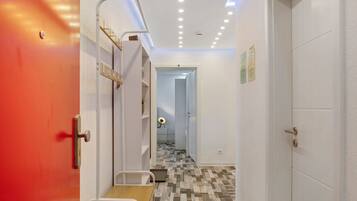 A hallway with a red door, a white door, and a staircase leading to a room with a bed.