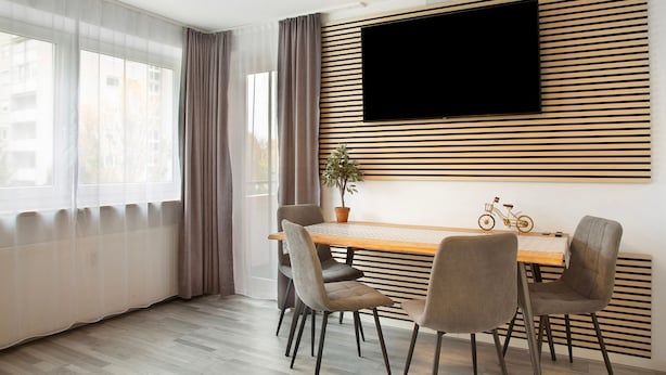 Ett modernt matområde med ett träbord, fyra stolar, en krukväxt och en väggmonterad TV.