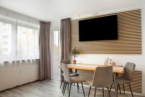 A modern dining area with a wooden table, four chairs, a potted plant, and a mounted TV.