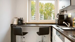Ett modernt kök med två barstolar, en kaffemaskin och ett fönster med utsikt över byggnader och träd.