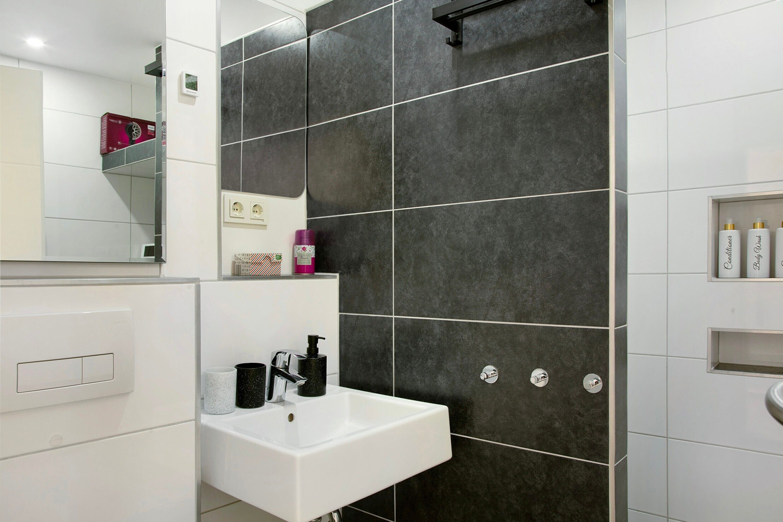 A modern bathroom with a white sink, dark tiled walls, and a mirror.