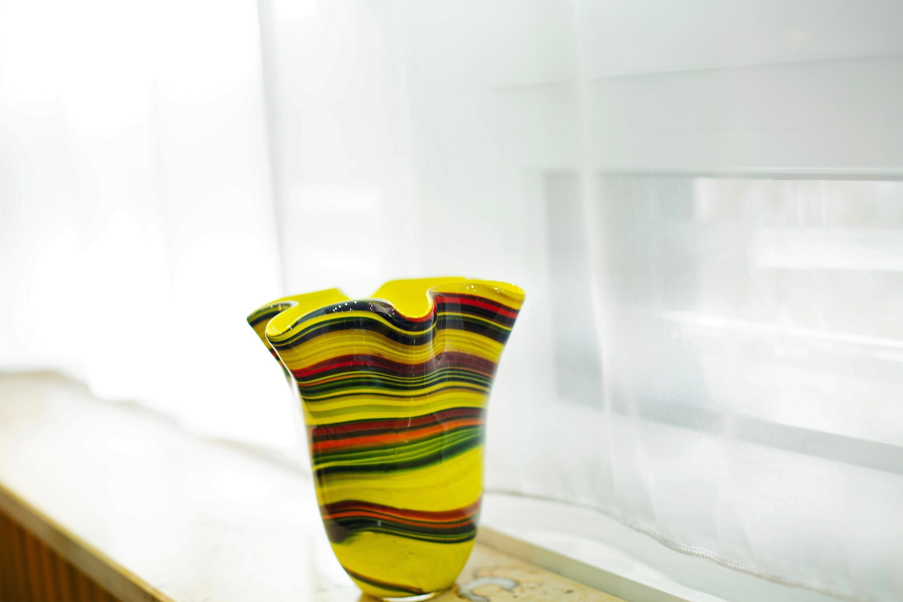 Un vase aux couleurs vives, posé sur un rebord de fenêtre.