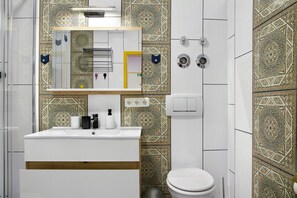 Ein Badezimmer mit einem weißen Waschbecken, einem Spiegel und einer Toilette. Die Wände sind mit aufwendigen Mustern gefliest.