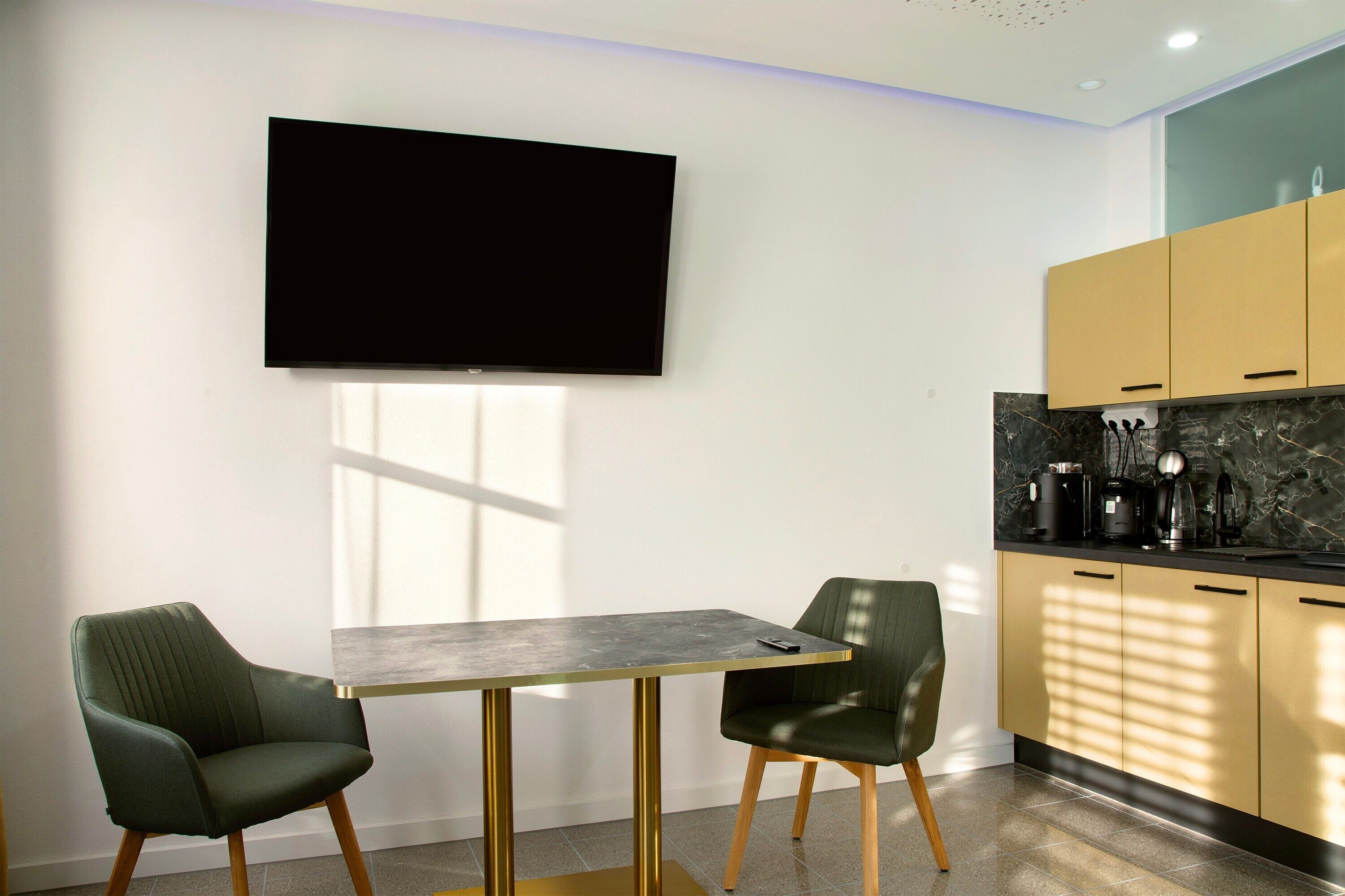 Una cucina moderna con una TV a schermo piatto, due sedie, un tavolo e pensili in legno.