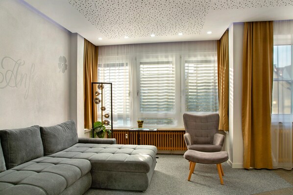 A modern living room with a sectional sofa, a single armchair, a floor lamp, and a radiator.