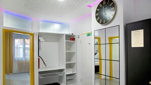 A room with a white shelving unit, a black clock, and a door with a yellow stripe. - Apartment 'Neuburg 1 - New' with Wi-Fi (Neuburg an der Donau)