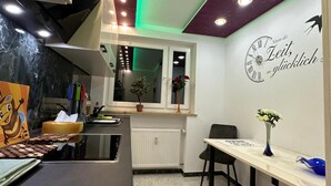 A modern kitchen with a marble countertop, a dining area with a table and chairs, a clock on the wall, and a window with a plant.