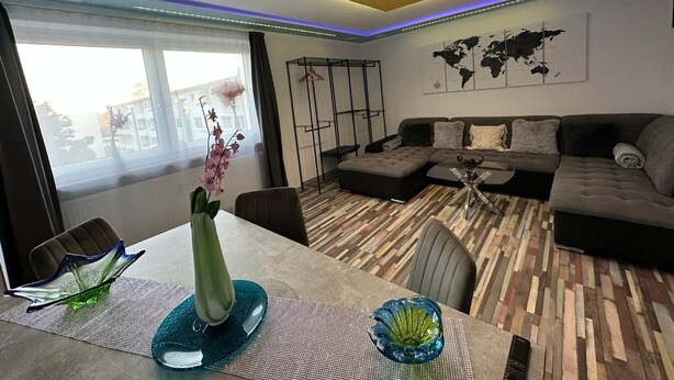 A modern living room with a sectional sofa, a dining table with chairs, a decorative vase, and a world map on the wall.