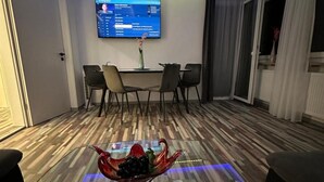 A modern living room with a TV on the wall, a glass coffee table with fruit, and a wooden floor.