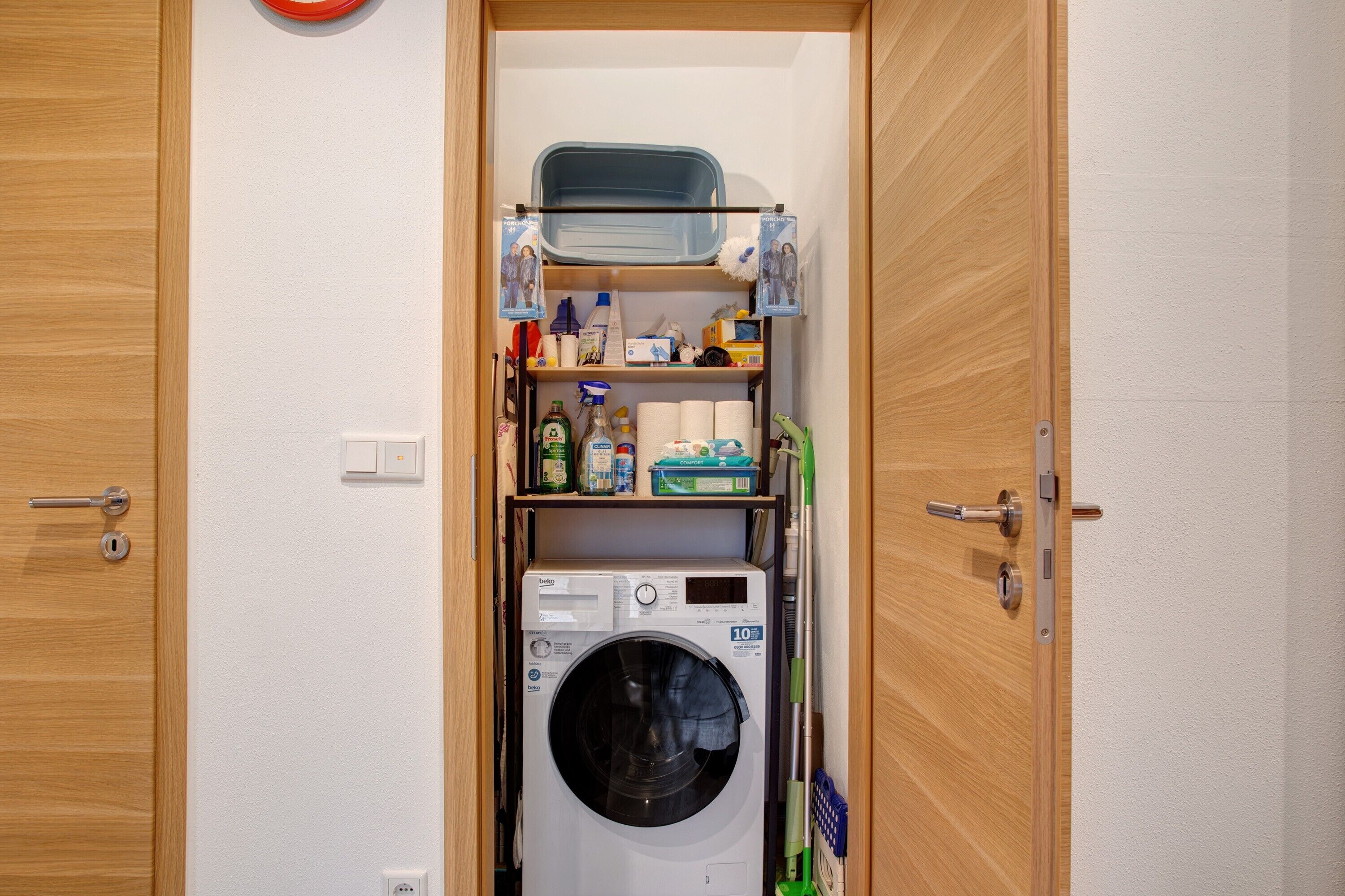 Une petite buanderie comprenant un lave-linge, des étagères pour les produits de toilette et un petit espace de rangement.