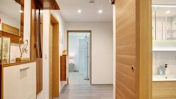 A hallway with wooden flooring, a mirror, a door, and a bathroom with a sink and mirror.