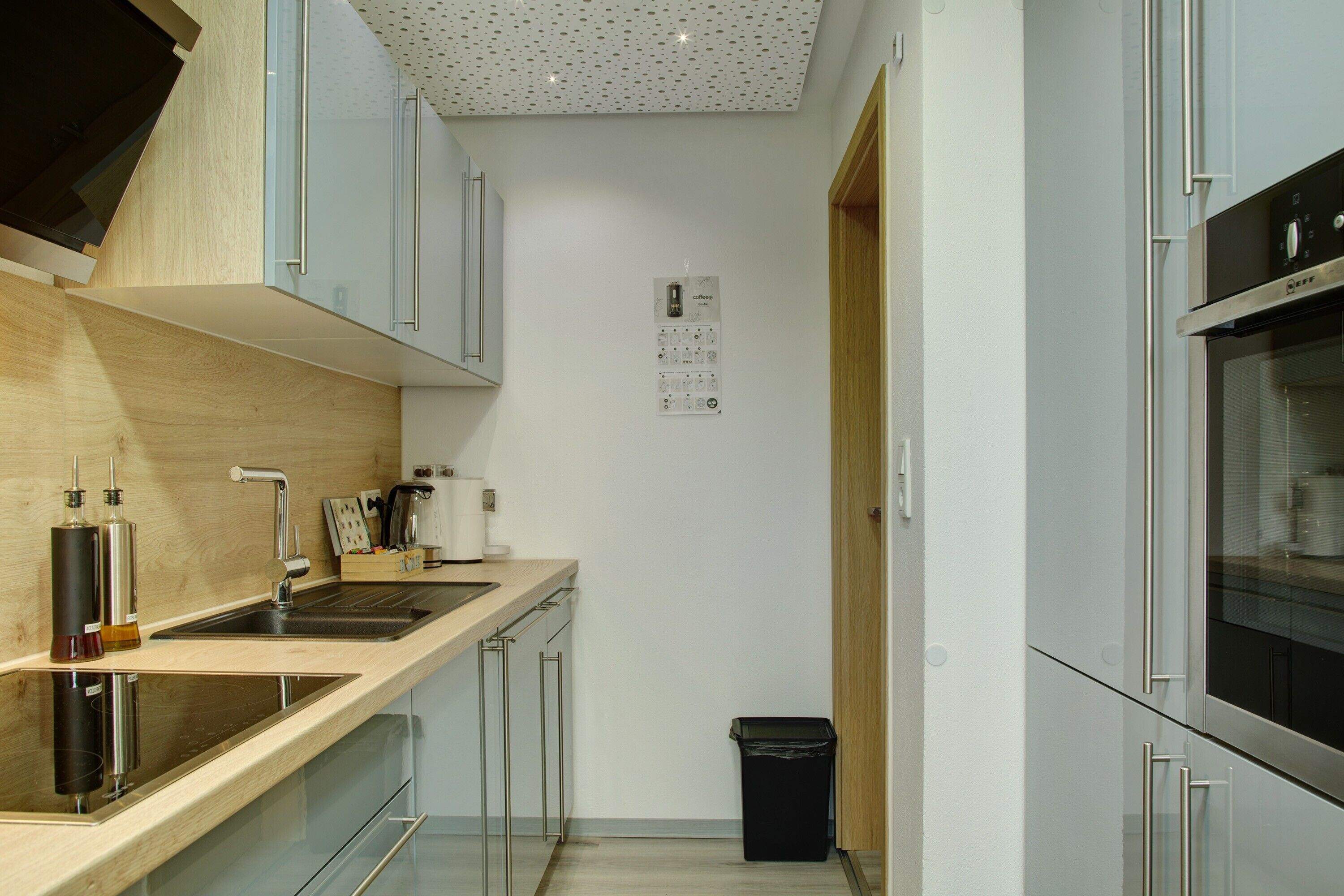 A modern kitchen with stainless steel appliances, a wooden countertop, and a black trash bin.
