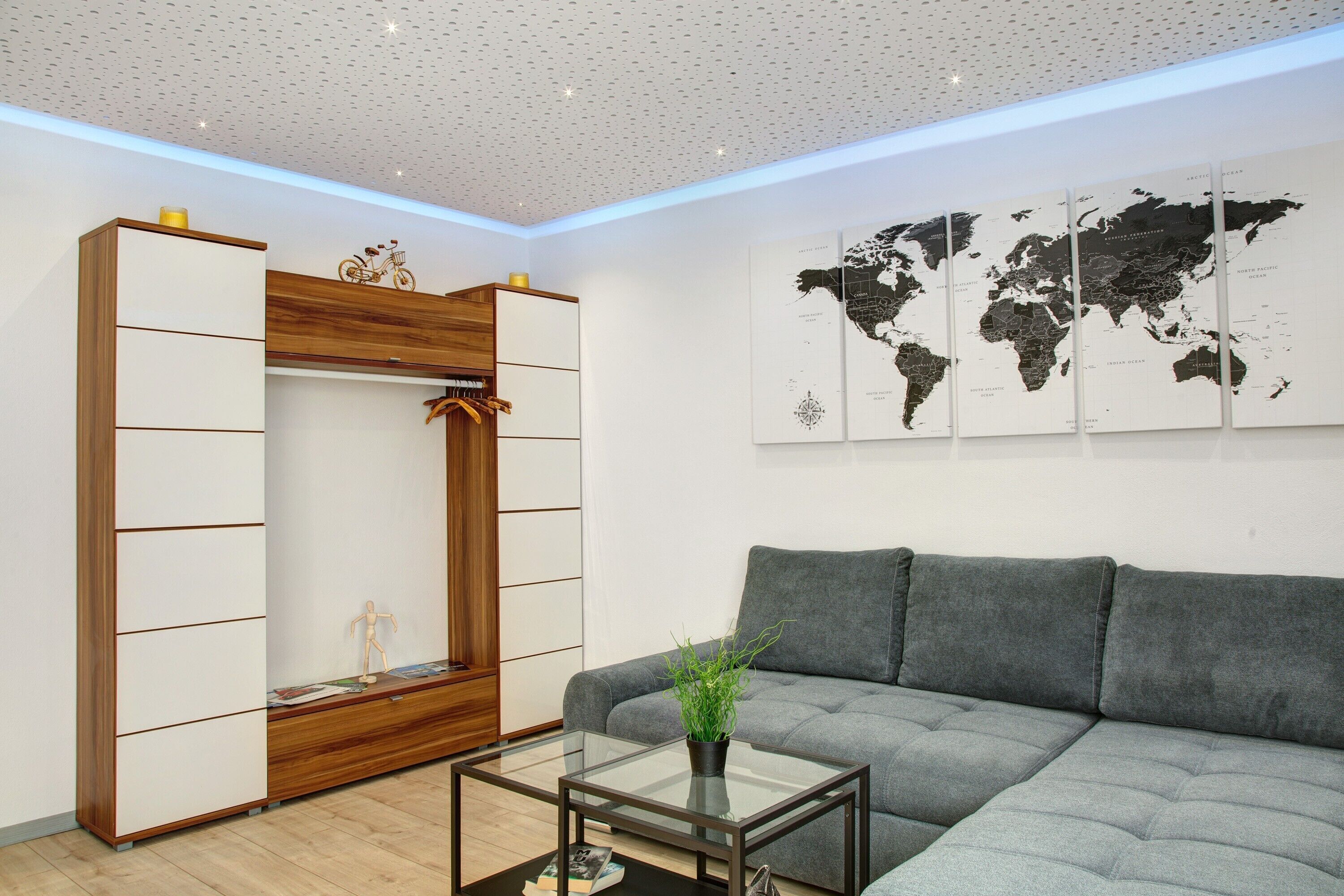 Una sala de estar moderna con un sofá gris, una mesa de centro de vidrio, un armario de madera y un mapa del mundo en la pared.