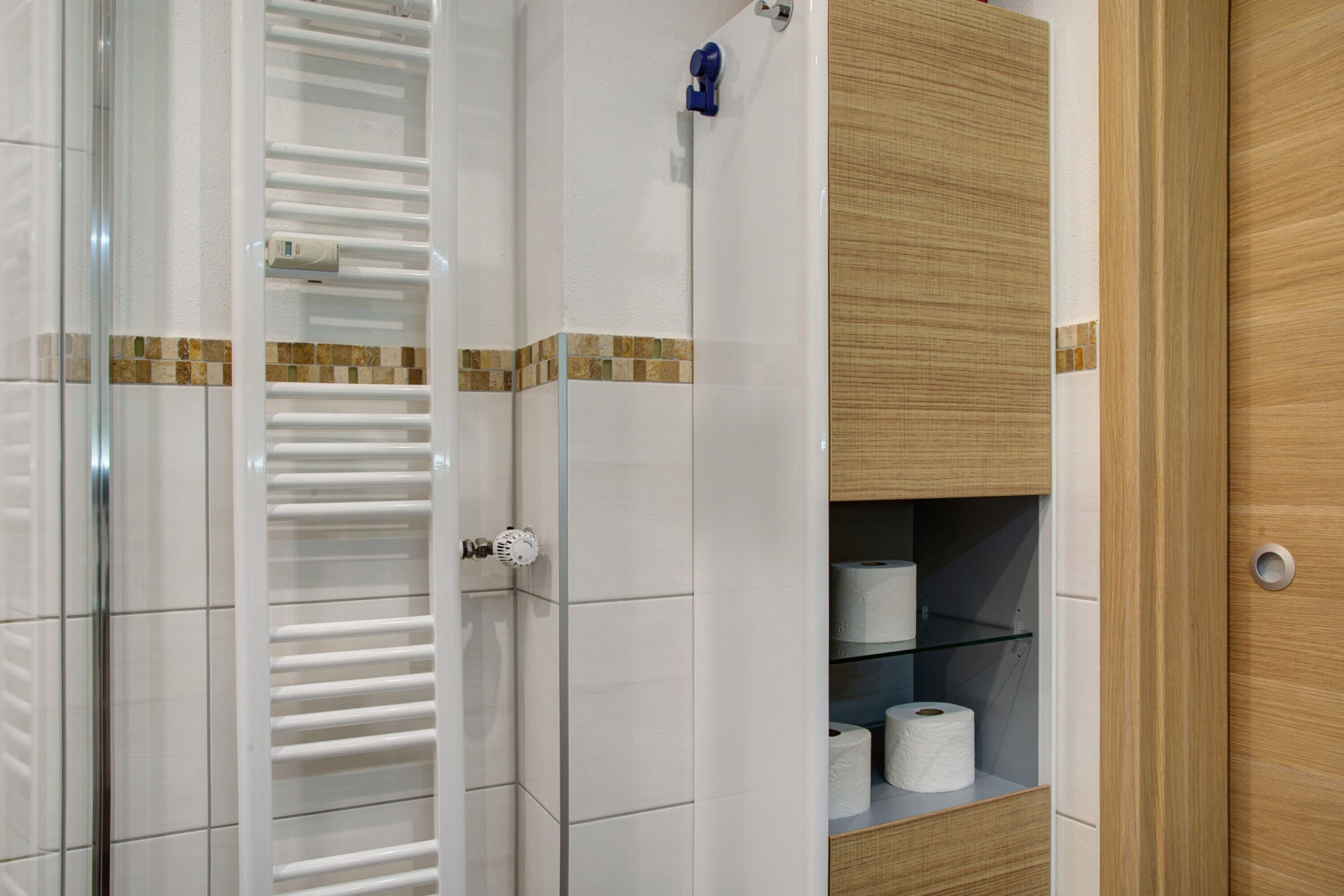 Ein Badezimmer mit Duschkabine aus Glas, Toilettenpapierhalter und einer Holzeinrichtung mit Regalen.
