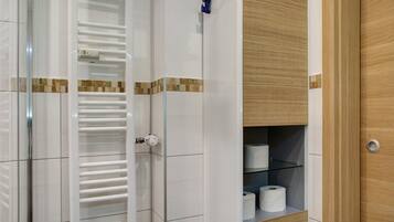 Ein Badezimmer mit Duschkabine aus Glas, Toilettenpapierhalter und einer Holzeinrichtung mit Regalen.