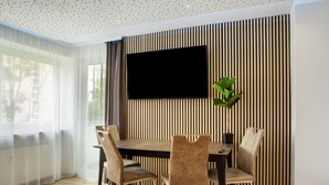 Ein moderner Essbereich mit Holztisch, Stühlen, einem Wand-Fernseher und einem Blumentopf.