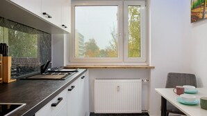 Una cocina moderna con ventana, armarios blancos, encimera negra y un comedor con mesa y sillas.