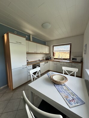 Ett kompakt kök med vita skåp, en spis och en mikrovågsugn. Där finns ett matbord med två stolar och en dekorativ tallrik.