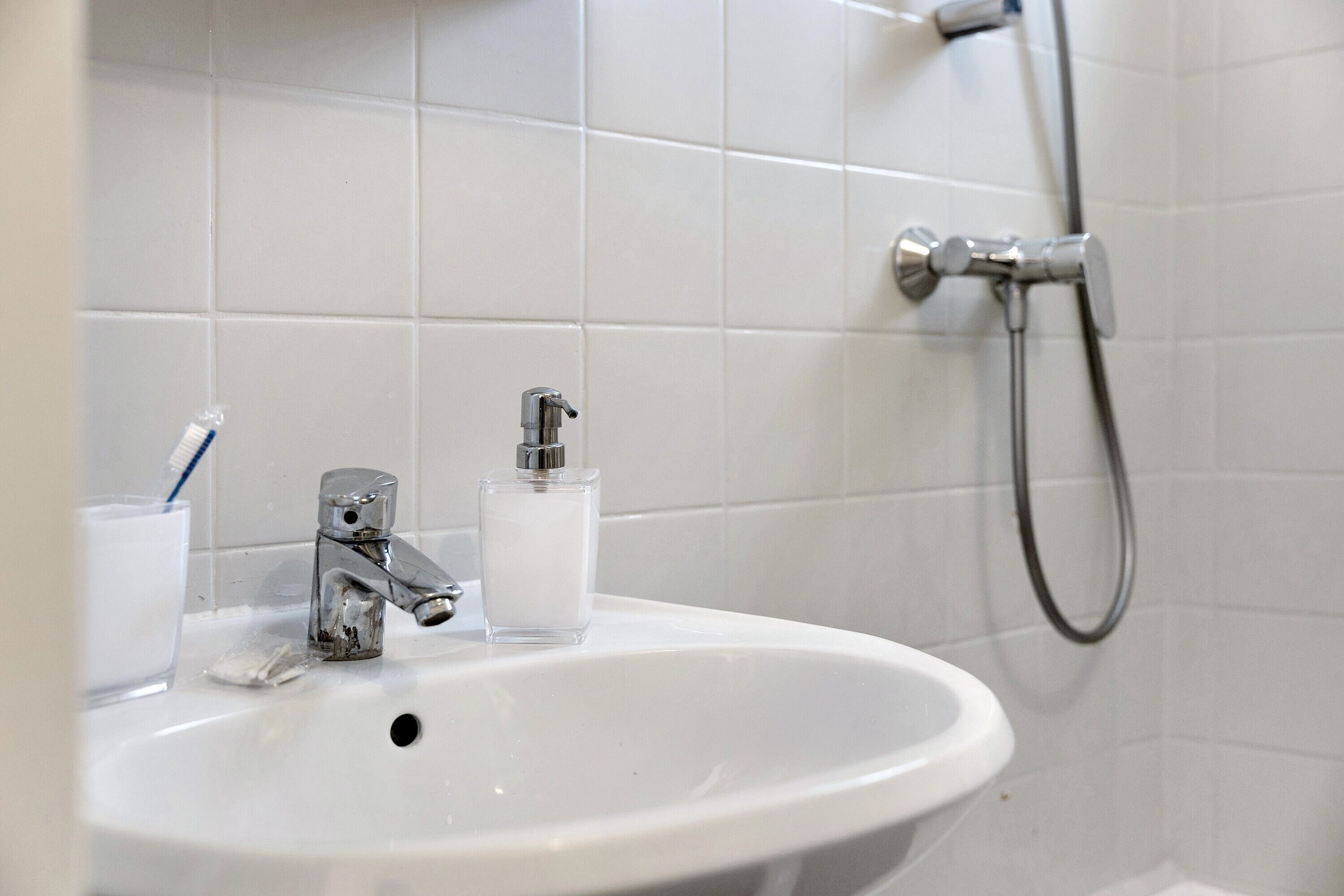 A bathroom sink with a faucet, a glass of water, and a soap dispenser.