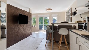 Una cocina moderna con una televisión de pantalla plana, taburetes de bar y una zona de comedor con un ventanal grande.