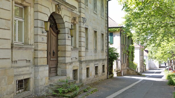 Un edificio de piedra histórico con una puerta de madera grande, varias ventanas y una calle estrecha.