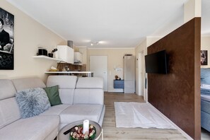 Uma sala de estar moderna com sofá, televisão de tela plana, espaço de cozinha e corredor que dá para um quarto.
