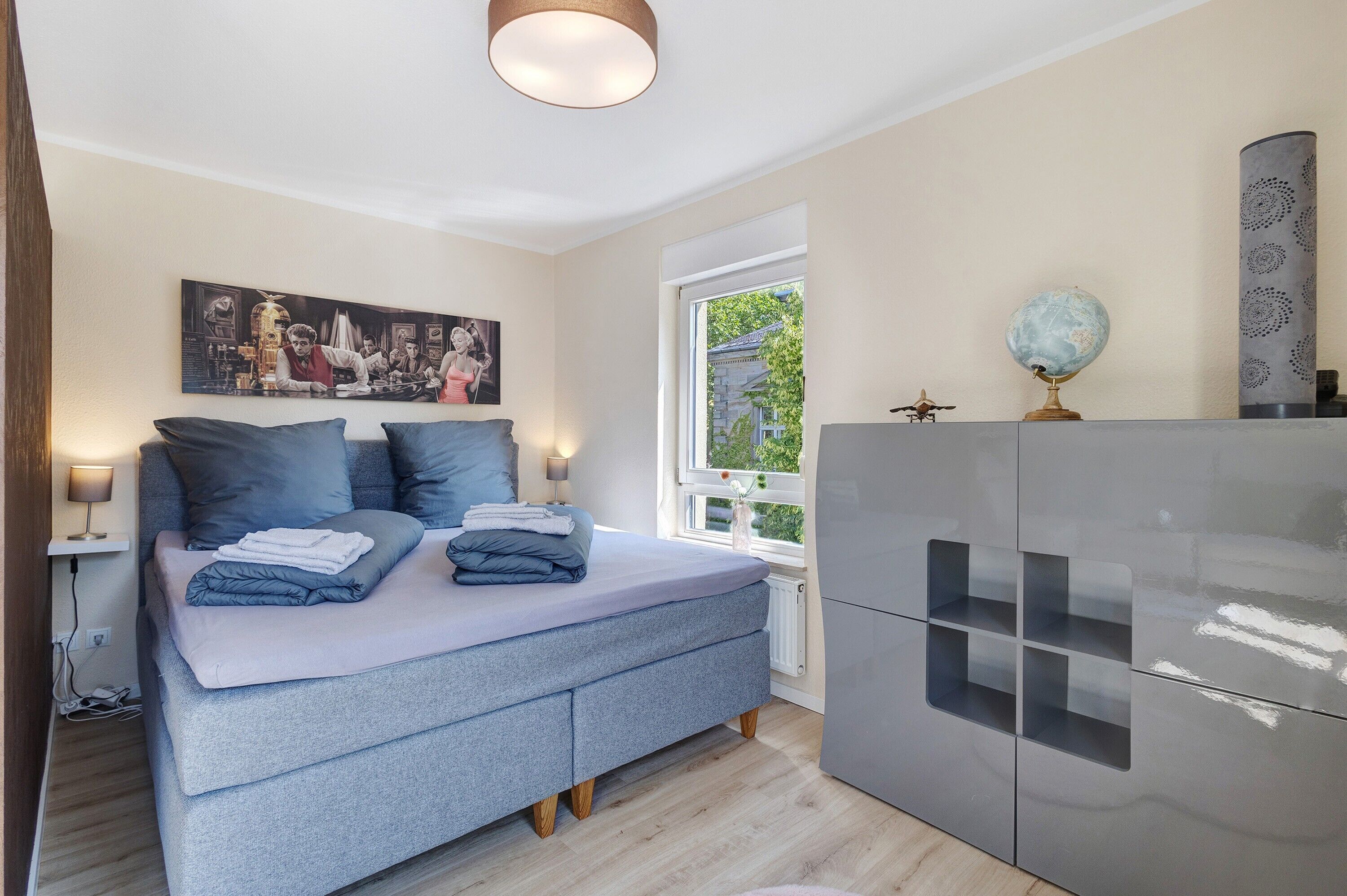 Ein Schlafzimmer mit einem Bett, Nachttischlampen, einem Fenster, einem Globus und einem Schrank.