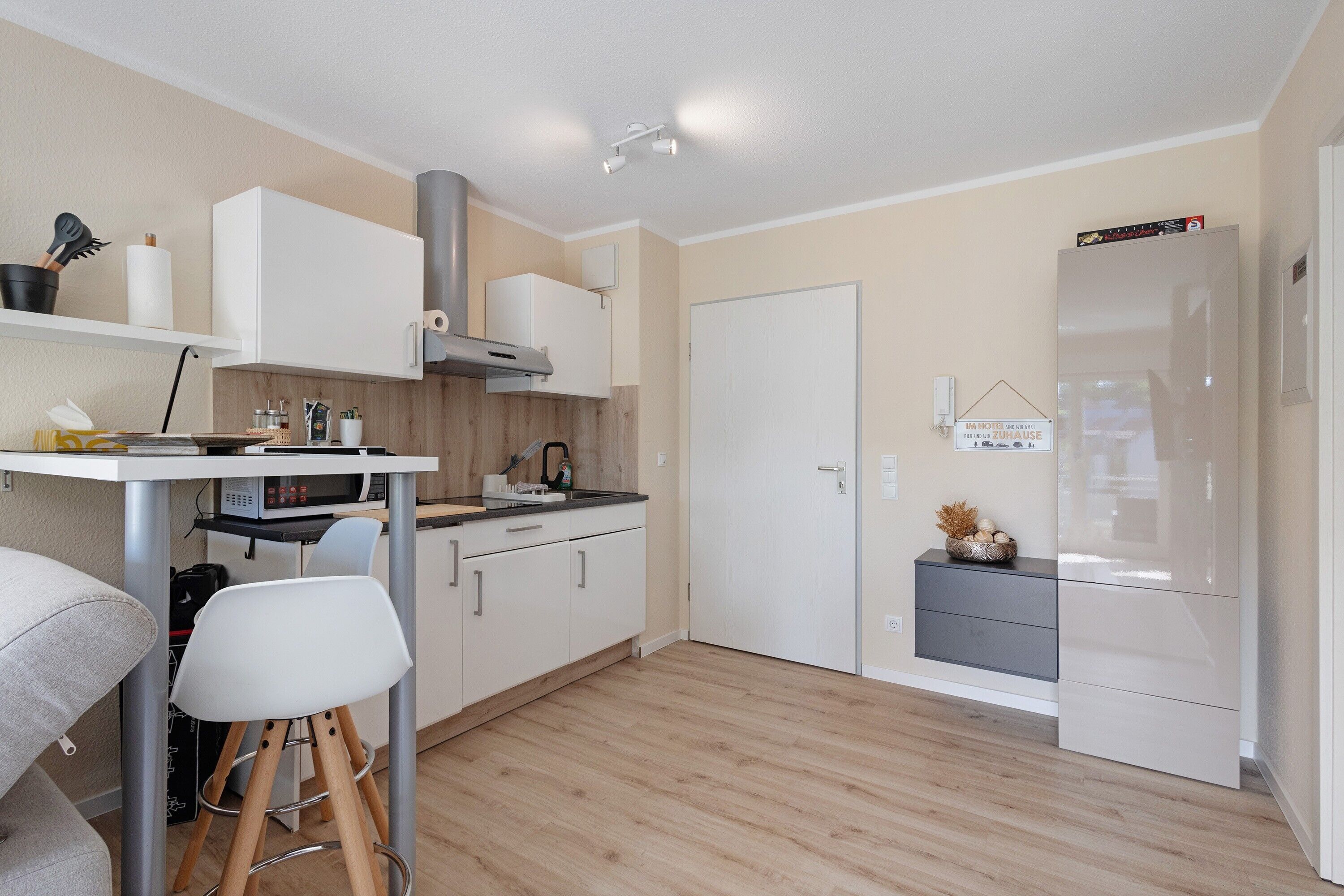 A modern kitchen with white cabinets, a stainless steel range hood, a microwave, and a refrigerator.