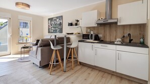 Una cocina moderna con armarios blancos, un microondas y una estufa. Hay un comedor con un sofá y dos sillas.