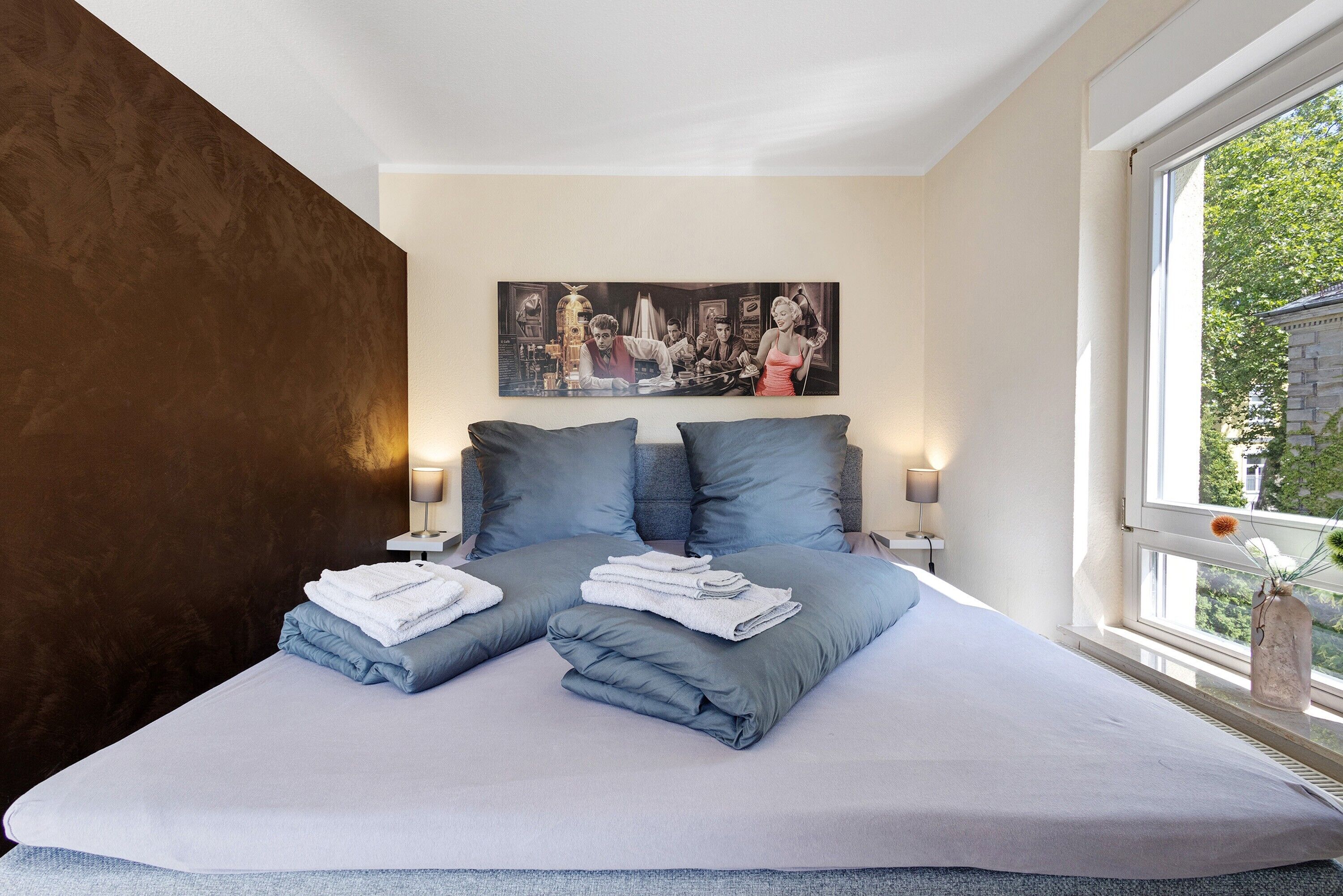 Ein Schlafzimmer mit Bett, Kissen, einem Gemälde und einem Fenster.