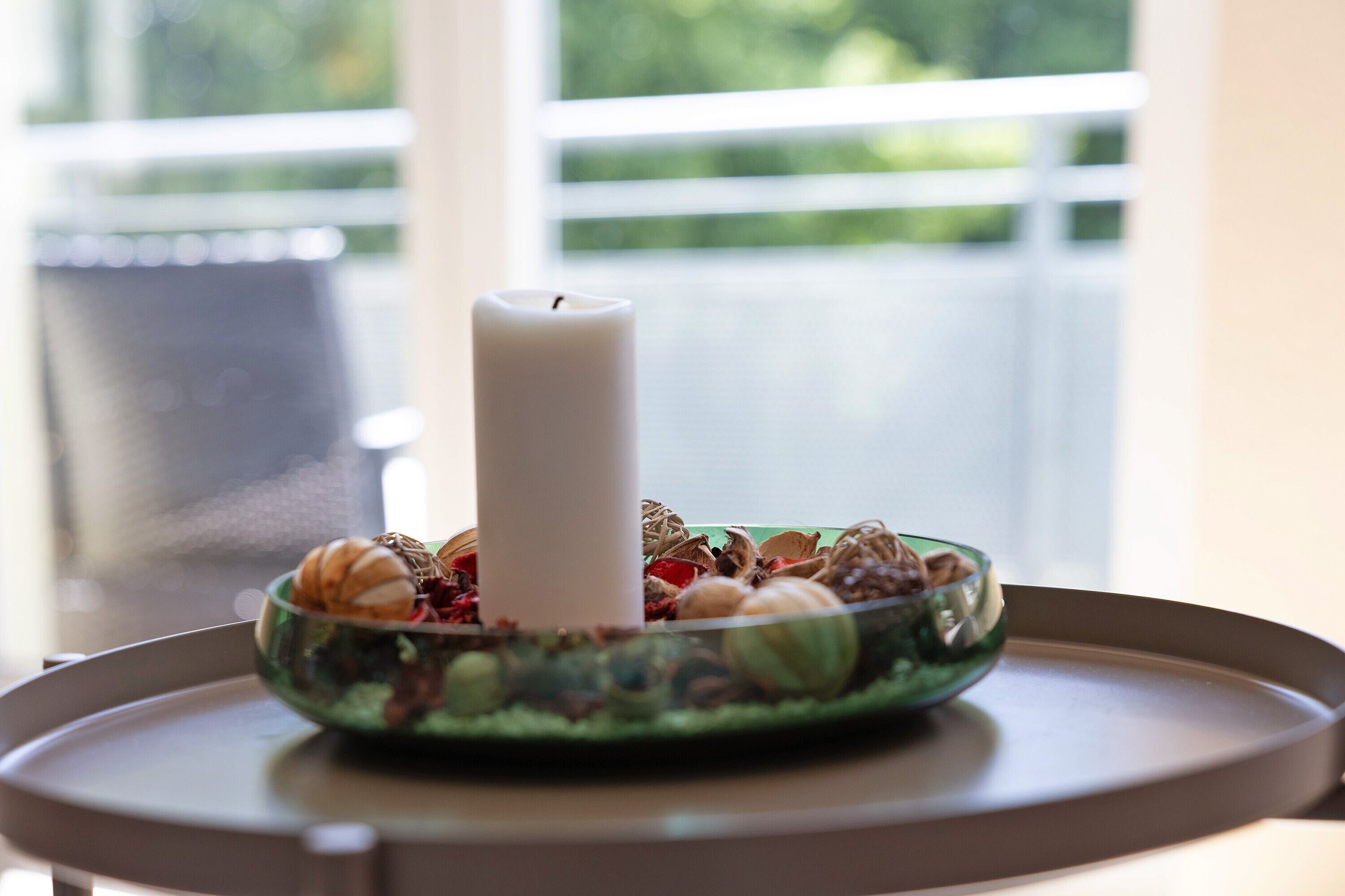 A candle in a bowl on a table with a window in the background.
