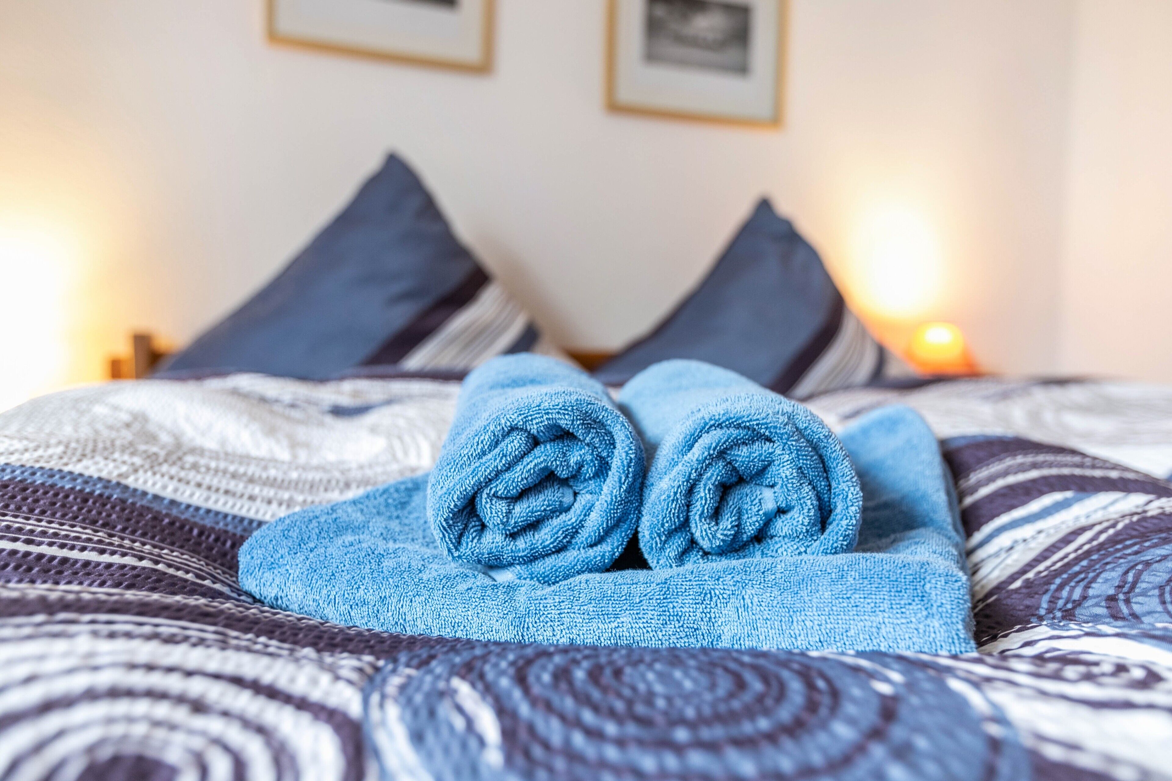 A bed with rolled blue towels, a patterned bedspread, and two pillows.