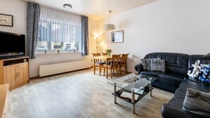 A living room with a television, a glass coffee table, a sofa, a dining table with chairs, and a window with curtains. - Apartment 'Groth's' with Shared Terrace, Shared Garden and Wi-Fi (Lunden)