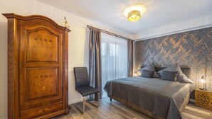 A bedroom with a large wooden wardrobe, a bed with a grey quilt, and a patterned wall.