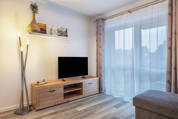 Una sala de estar moderna con un televisor de pantalla plana sobre una consola de madera, un jarrón y un marco de fotos en la pared.