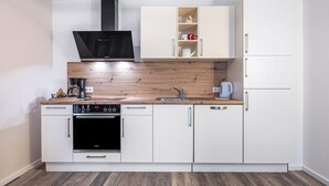 A modern kitchen with white cabinetry, a wooden countertop, a built-in oven, and a black range hood.