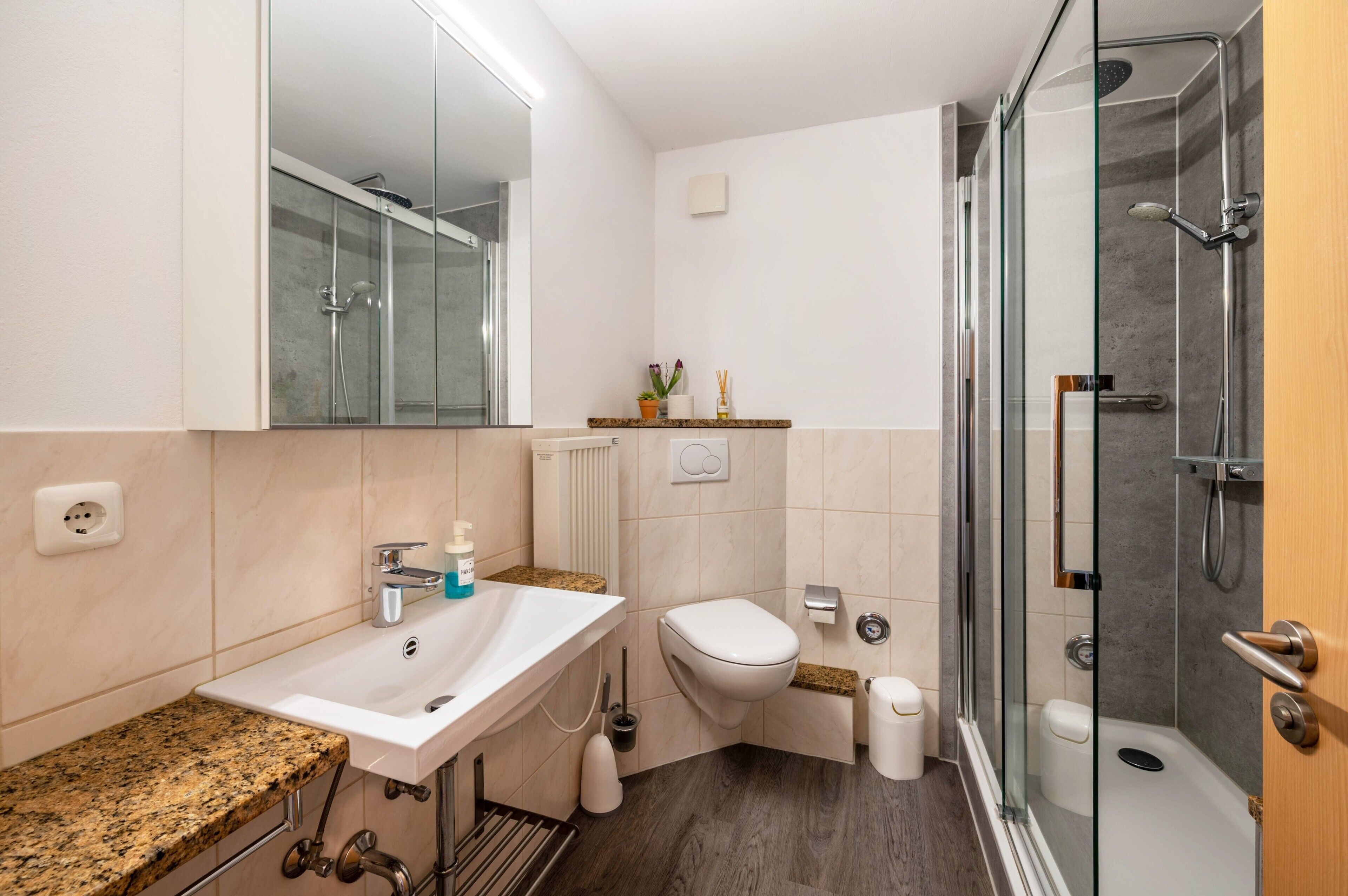 A modern bathroom with a glass shower enclosure, a sink with a granite countertop, a toilet, and a mirror.