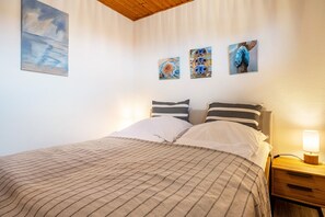 Un lit bien fait, avec une literie à rayures, une table de chevet avec une lampe, et trois tableaux accrochés au mur.