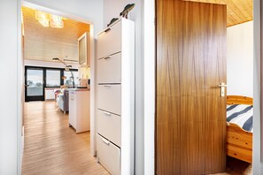 Une cuisine moderne avec un réfrigérateur blanc, un plancher en bois et une vue sur l’extérieur grâce à une porte vitrée.