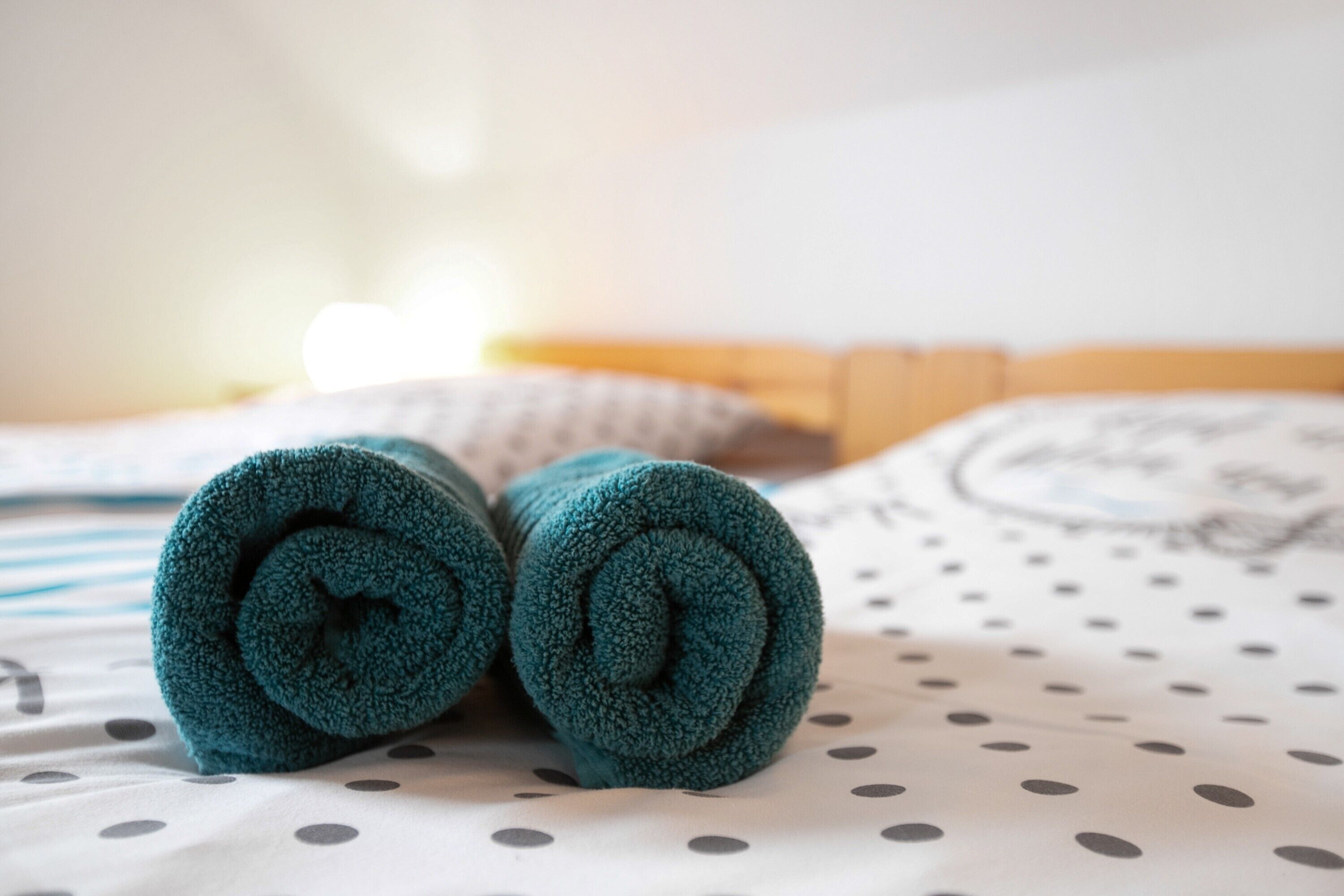 Ein Bett mit einem Löcher-Muster-Laken, einem eingerollten türkisfarbenen Handtuch und einem Kissen mit einem kreisförmigen Muster.