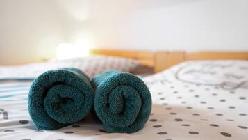Ein Bett mit einem Löcher-Muster-Laken, einem eingerollten türkisfarbenen Handtuch und einem Kissen mit einem kreisförmigen Muster.