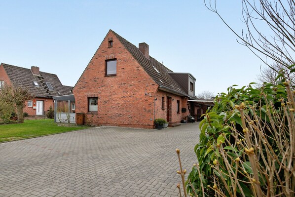 A red brick building with a sloped roof, a paved driveway, and a small garden area.
