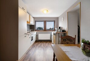 A compact kitchen with a radiator, wooden flooring, a dining table with a placemat, and a window with a view.