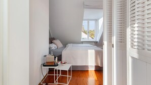 Une chambre à coucher avec un lit, une table de chevet, une fenêtre avec des stores et une vue sur l’extérieur.