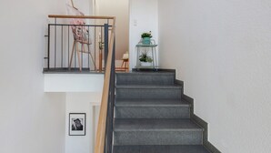 Un escalier avec une main courante en bois et une rampe en métal noir, menant à un palier où se trouvent un tableau et une petite table avec des plantes.
